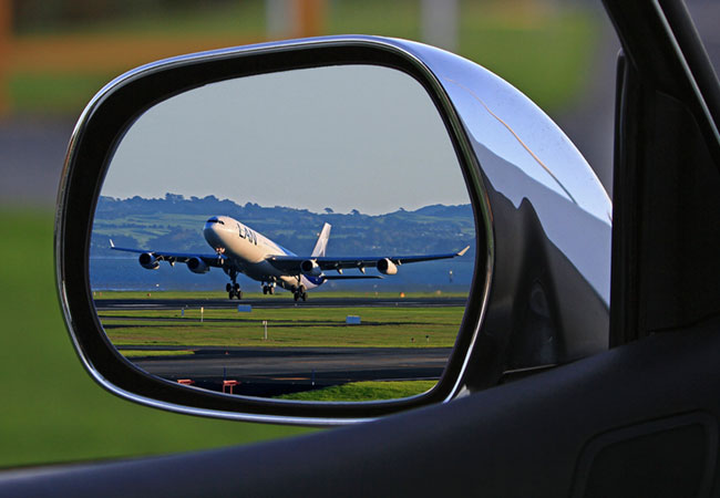 Car at the airport with plane in the rearview mirror